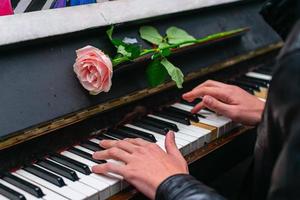 The hands of a street musician playing the piano on which lies a rose photo