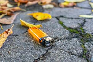 El encendedor de bolsillo naranja perdido yace en el camino entre las hojas caídas de otoño foto