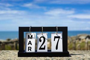 27 de marzo texto de fecha de calendario en marco de madera con fondo borroso del océano. foto