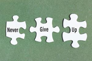 Motivational text on three pieces of white jigsaw puzzle on green background. photo