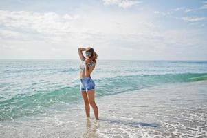 Beautiful model relaxing on a beach of sea, wearing on jeans short, leopard shirt and sunglasses. photo