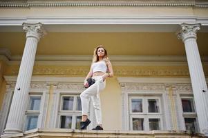 Stylish curly blonde model girl wear on white posing against old vintage house. photo