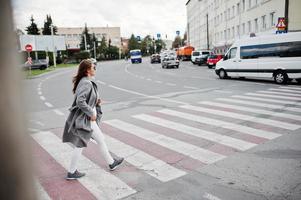 Girl in gray coat with sunglasses and handbag walking on the pedestrian crossing. photo