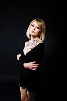 Studio portrait of blonde girl with originally make up on neck, wear on black dress at dark background. photo