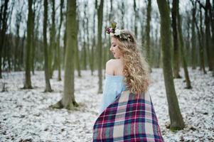 linda chica rubia rizada con corona en tela escocesa a cuadros en el bosque nevado en el día de invierno. foto