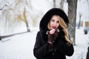 Elegance blonde girl in fur coat and red evening dress posed at winter snowy day. photo