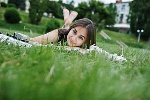 Portrait of a gorgeous woman in black polka dot dress laying next to the books on the blanket on the grass in the park. photo