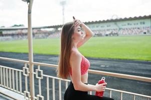 chica deportiva fitness en ropa deportiva en el estadio de deportes al aire libre. mujer sexy feliz con maqueta de botella deportiva. foto