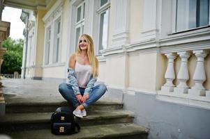 Blonde girl wear on jeans with backpack posed against vintage house. photo