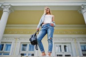 Blonde girl wear on jeans with backpack posed against vintage house. photo