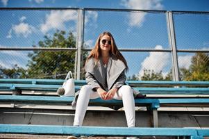 Girl in gray coat with sunglasses at small street stadium. photo