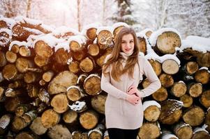 Beautiful brunette girl in winter warm clothing. Model on winter sweater near stump. photo