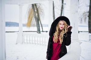 Elegance blonde girl in fur coat and red evening dress posed at winter snowy day. photo
