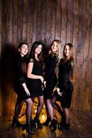 Four cute friends girls wear black dresses against large light christmas star decoration on wooden background. photo