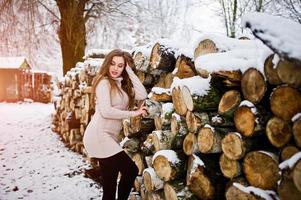 Beautiful brunette girl in winter warm clothing. Model on winter sweater near stump. photo