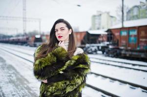 chica morena con abrigo de piel verde en la estación de la plataforma en el día de invierno. foto