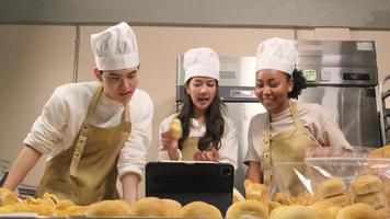 Young three chefs startup partners, small business blogger live streaming via mobile application technology, bakery sales online promotion, fresh bread, pastry food, and commercial kitchen cooking.