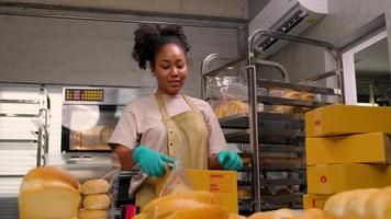 entrega de pequeñas empresas de inicio de panadería. una cocinera afroamericana está empacando pan y pasteles hechos a mano y recién horneados en cajas y enviando para compras de clientes en línea en la cocina culinaria. video