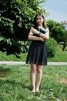 Portrait of a shy young woman in black polka dot dress holding books in the park. photo