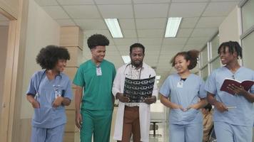 gruppe von praktikern, professioneller afroamerikanischer männlicher arzt mit jungen medizinstudenten team happy walk und besprechen diagnose röntgenfilm in der untersuchungsambulanz im krankenhaus. video