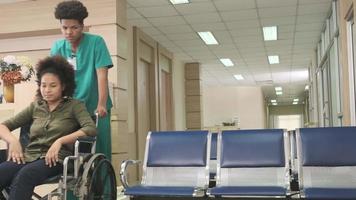 Young African American female doctor with stethoscope in uniform checks injury patient girl in wheelchair at outpatient accident clinic hospital, illness medical clinic examination, healthcare hall. video