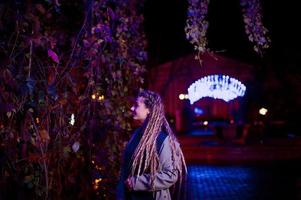 Girl with dreadlocks walking at night street of city against garland lights. photo