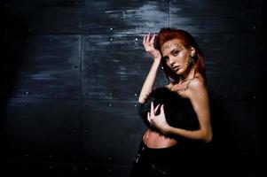 Fashion model red haired girl with originally make up like leopard predator against steel wall. Studio portrait. photo