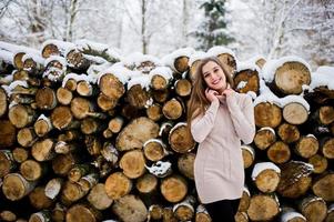 Beautiful brunette girl in winter warm clothing. Model on winter sweater near stump. photo