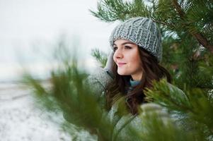 retrato de una chica gentil con abrigo gris y sombrero contra el árbol de año nuevo al aire libre. foto