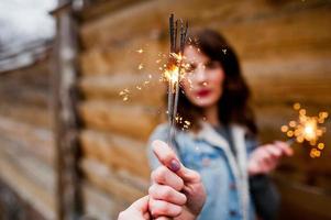 Portrait of brunette girl in jeans jacket with bengal lights in hands. photo