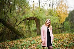 Young blonde girl at pink coat posed on autumn park. photo