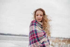 Curly blonde girl in checkered plaid against frozen lake at winter day. photo