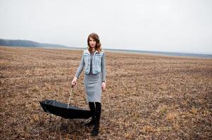 Portrait of brunette curly girl in jeans jacket with black umbrella at field. photo