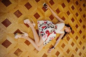 retrato de una joven deslumbrante con un vestido precioso tirado en el suelo con su smartphone. foto