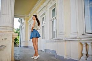 Curly stylish girl wear on blue jeans skirt, blouse posed near old vintage house. photo