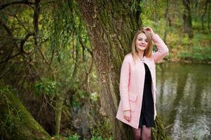 Young blonde girl at pink coat posed on autumn park. photo