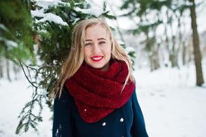 Blonde girl in red scarf and coat walking at park on winter day. photo