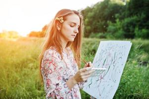 Portrait of an attractive young woman in long dress painting with watercolor in nature. photo