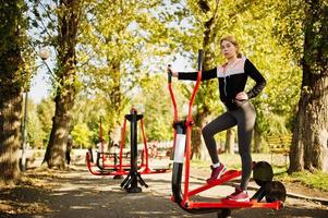 la joven tiene el entrenamiento y hace ejercicio al aire libre en simuladores callejeros. deporte, fitness, concepto de entrenamiento callejero. foto