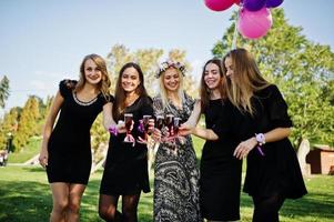 Five girls wear on black with balloons drinking red champagne at hen party. photo