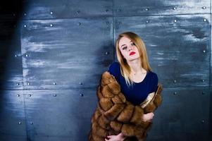 Elegante blonde girl wear on fur coat and combi dress posed against steel wall on studio. photo