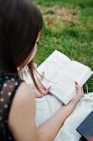 Portrait of a beautiful woman in black polka dot dress laying on the blanket on the grass and reading. photo