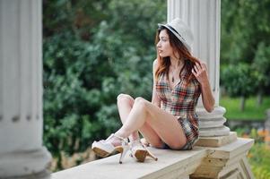 Amazing long legs with hig heels girl wear on hat sitting near vintage building columns. photo