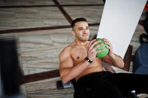 Muscular arab man training in modern gym. Fitness arabian men with naked torso doing exercises with ball. photo