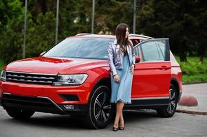 Outdoor photo of gorgeous woman posing near orange suv car with open door.