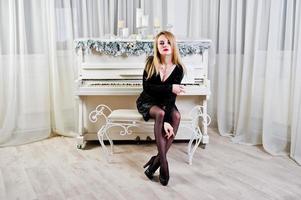Elegante blonde girl wear on black dress against piano with christmas decoration. photo