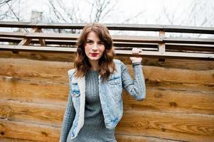 Portrait of brunette curly girl in jeans jacket against wooden wall. photo