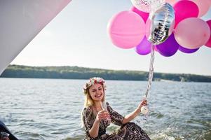 Blonde girl in wreath sitting on yacht at hen party with champagne. photo