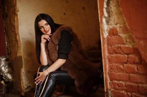 Fashion outdoor photo of gorgeous sensual woman with dark hair in elegant clothes and luxurious fur coat at old street with grunge walls.