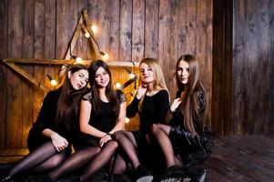 Cuatro lindas amigas usan vestidos negros contra una gran decoración de estrellas de Navidad claras sobre fondo de madera. foto